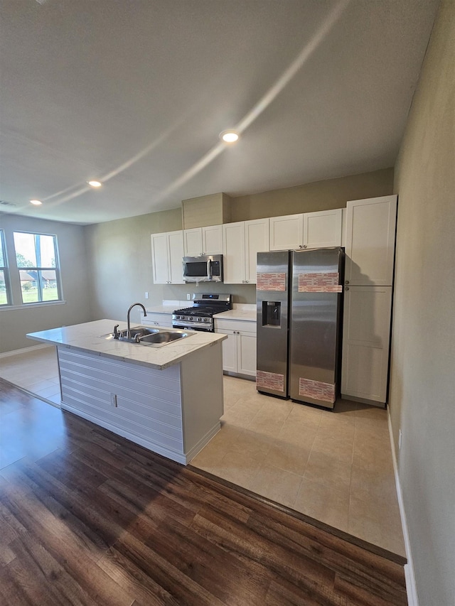 kitchen with white cabinets, sink, light hardwood / wood-style flooring, an island with sink, and stainless steel appliances