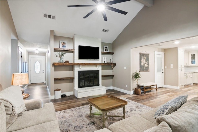 living room featuring a brick fireplace, beam ceiling, ceiling fan, and light wood-type flooring