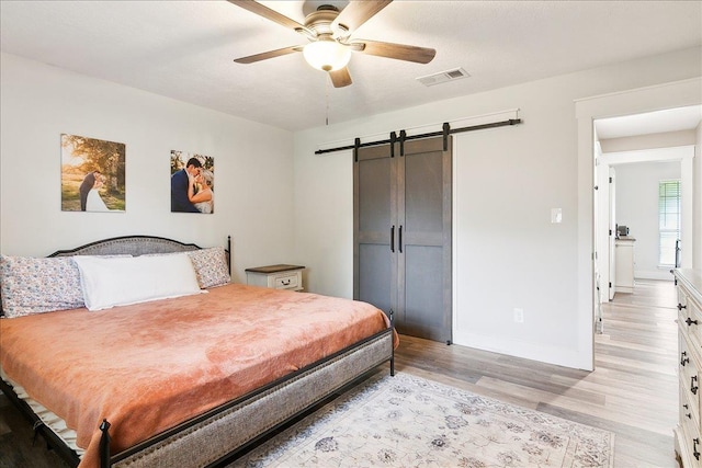 bedroom featuring a barn door, ceiling fan, and light wood-type flooring