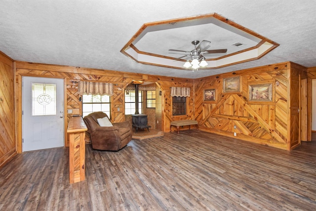 sitting room featuring a wood stove, ceiling fan, dark hardwood / wood-style flooring, a textured ceiling, and wooden walls