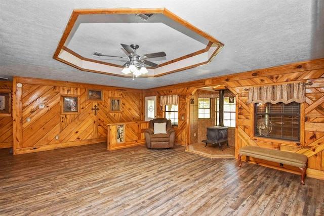 interior space featuring a wood stove, ceiling fan, a textured ceiling, wooden walls, and hardwood / wood-style flooring