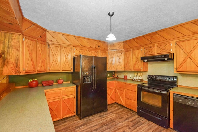 kitchen featuring wooden walls, hanging light fixtures, black appliances, and light hardwood / wood-style floors