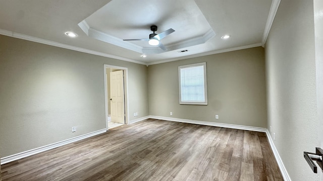 empty room with a raised ceiling, crown molding, hardwood / wood-style flooring, and ceiling fan