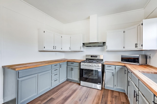 kitchen featuring butcher block countertops, white cabinetry, light hardwood / wood-style floors, gas stove, and wall chimney exhaust hood