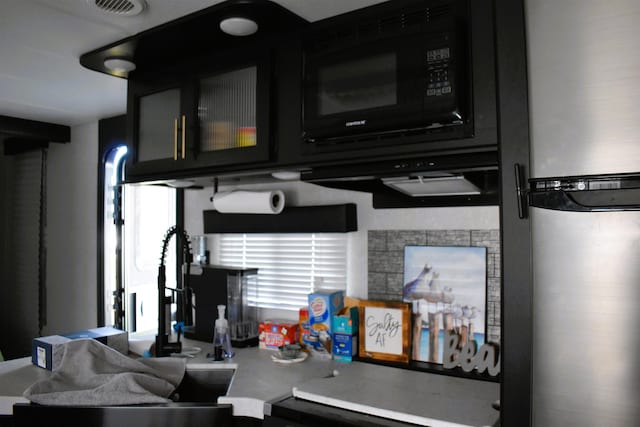 interior space featuring black microwave, visible vents, light countertops, freestanding refrigerator, and glass insert cabinets