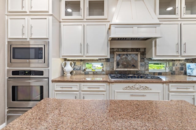 2425 Amberwood Dr, Beaumont, TX 77713 - kitchen with stainless steel appliances, custom exhaust hood, glass insert cabinets, and white cabinetry