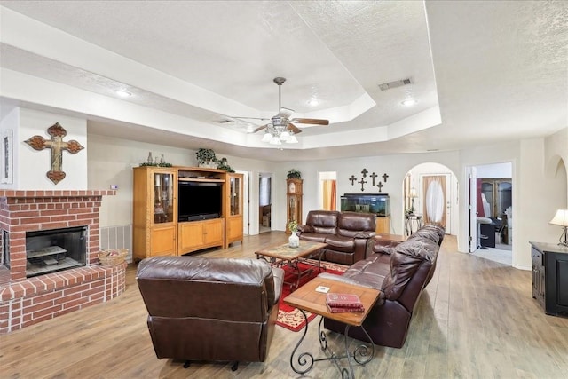 living room featuring light hardwood / wood-style flooring, a textured ceiling, a fireplace, and a tray ceiling