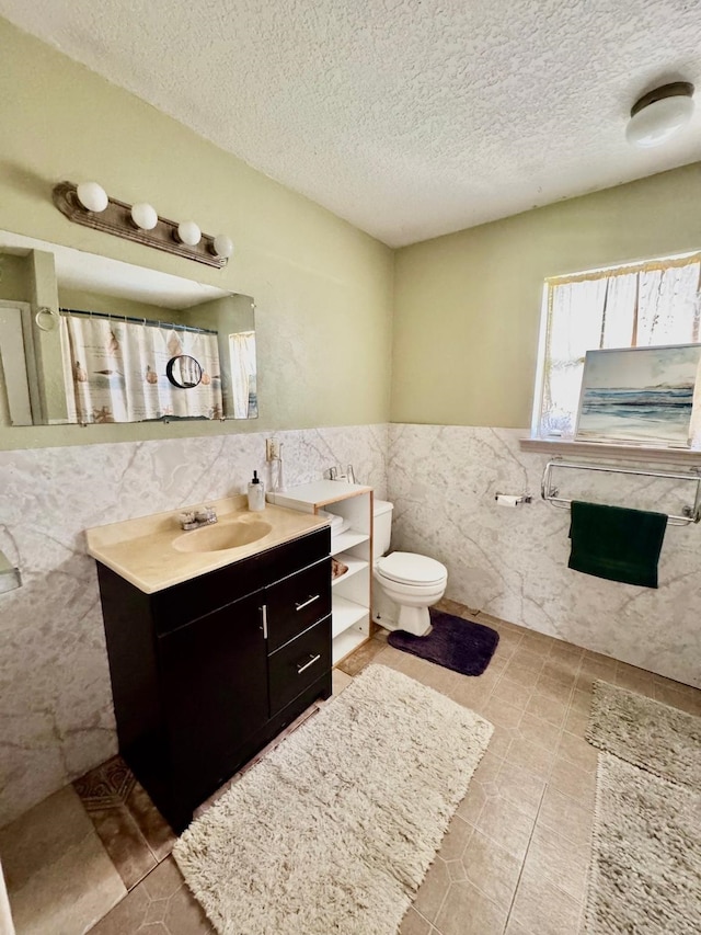 bathroom with tile walls, a textured ceiling, vanity, toilet, and tile patterned flooring