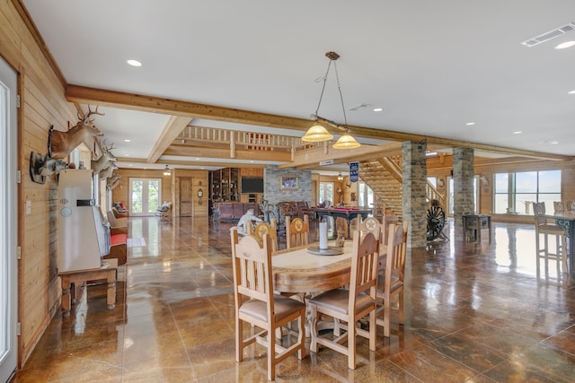 dining room featuring beam ceiling, rustic walls, wood walls, and ornate columns