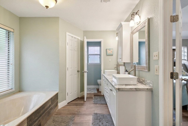 bathroom featuring vanity, toilet, wood-type flooring, and tiled bath