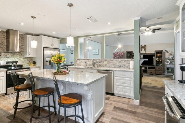 kitchen with wall chimney exhaust hood, stainless steel appliances, backsplash, pendant lighting, and white cabinets