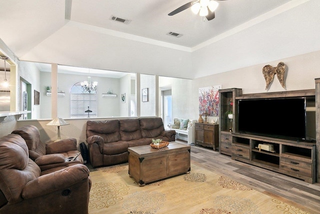 living room featuring ceiling fan with notable chandelier, a tray ceiling, light hardwood / wood-style flooring, and a healthy amount of sunlight