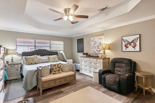 bedroom with a raised ceiling, ceiling fan, dark wood-type flooring, and crown molding