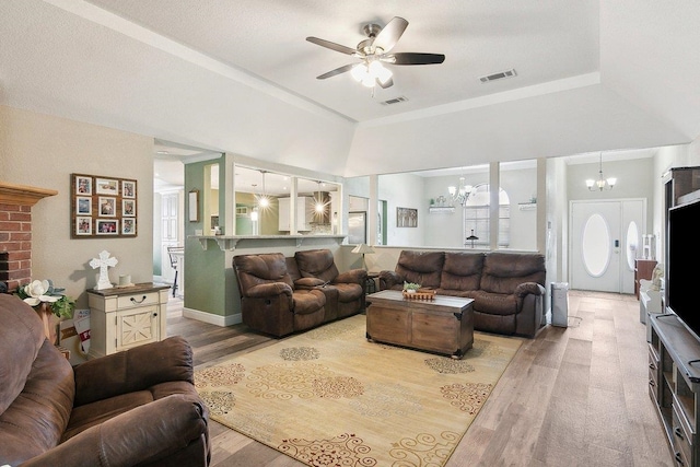 living room with ceiling fan with notable chandelier, a raised ceiling, and light hardwood / wood-style flooring