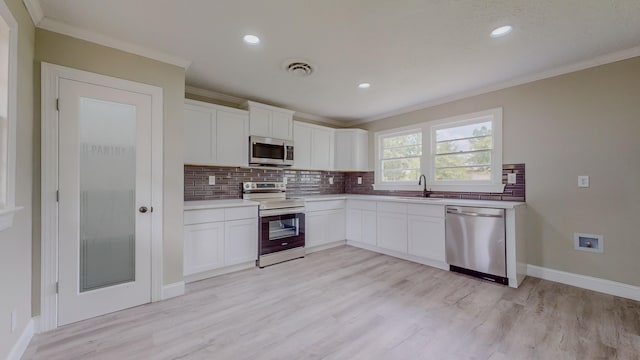 kitchen with white cabinetry, sink, stainless steel appliances, backsplash, and ornamental molding