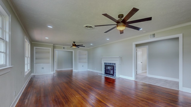 unfurnished living room with built in shelves, a textured ceiling, crown molding, dark wood-type flooring, and a tiled fireplace