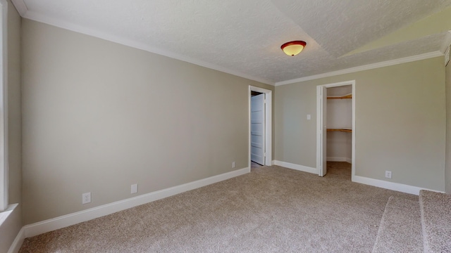 unfurnished bedroom with lofted ceiling, light carpet, a walk in closet, ornamental molding, and a textured ceiling