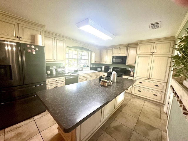 kitchen featuring crown molding, black appliances, light tile patterned floors, cream cabinetry, and a kitchen island