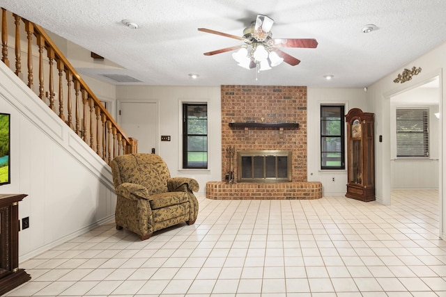 1911 Huntsman St, Orange, TX 77632 - living room featuring a textured ceiling, a ceiling fan, a brick fireplace, stairway, and light tile patterned floors