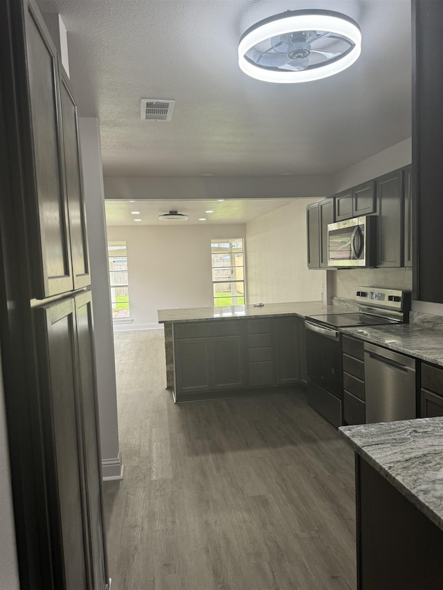 kitchen featuring dark hardwood / wood-style floors, light stone counters, kitchen peninsula, and appliances with stainless steel finishes