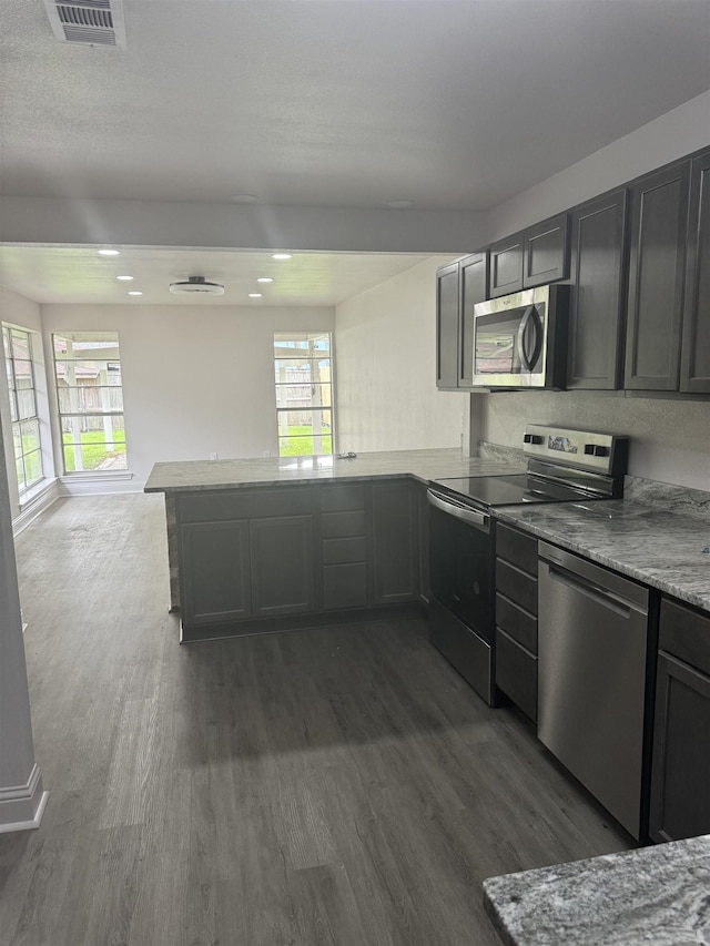 kitchen with kitchen peninsula, light stone counters, dark hardwood / wood-style flooring, and stainless steel appliances