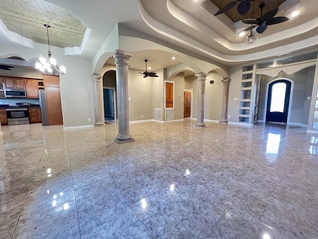 interior space featuring ceiling fan with notable chandelier, a towering ceiling, a tray ceiling, and decorative columns