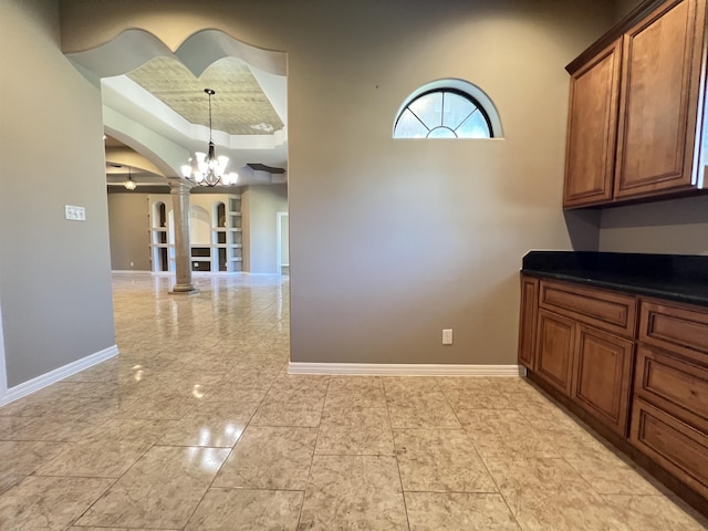 kitchen with an inviting chandelier, a tray ceiling, decorative light fixtures, and ornate columns