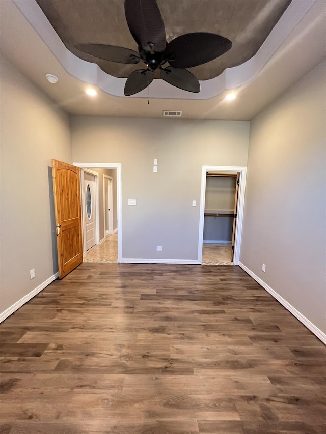 unfurnished bedroom featuring dark wood-type flooring, a walk in closet, a tray ceiling, a closet, and ceiling fan