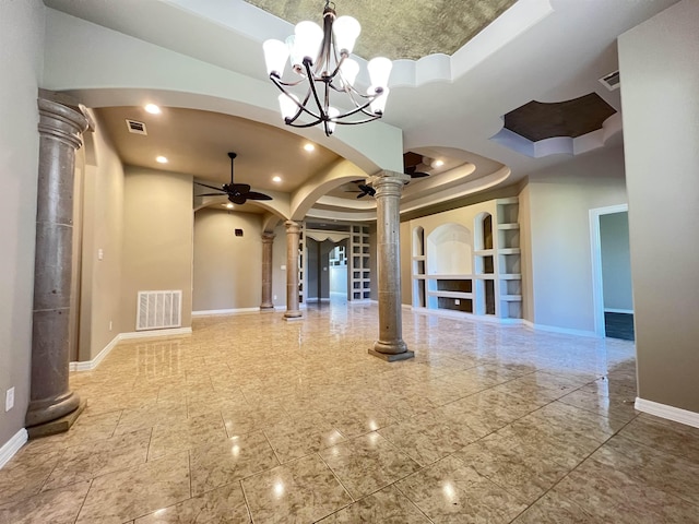 empty room featuring ornate columns, a tray ceiling, built in features, ceiling fan with notable chandelier, and a high ceiling