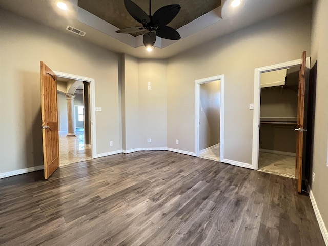 unfurnished bedroom featuring ceiling fan, a walk in closet, a raised ceiling, and a closet