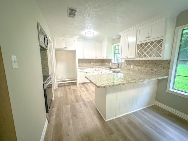 3640 Whippoorwill St, Orange, TX 77630 - kitchen with light wood-type flooring, a peninsula, white cabinets, tasteful backsplash, and appliances with stainless steel finishes