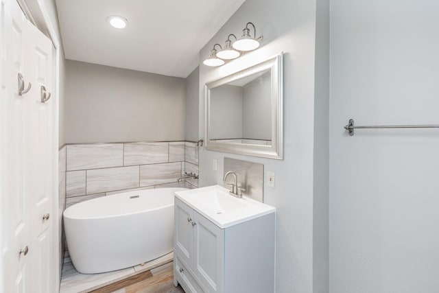 bathroom featuring vanity, hardwood / wood-style flooring, tile walls, and a tub