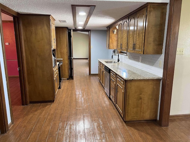 kitchen featuring a textured ceiling, hardwood / wood-style flooring, sink, stainless steel dishwasher, and backsplash