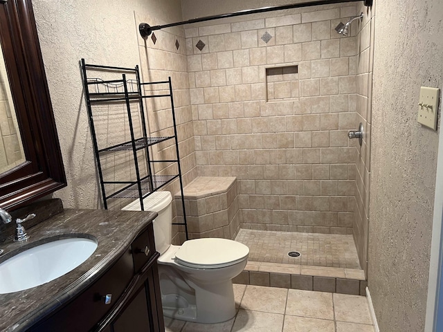 bathroom with toilet, tile patterned flooring, a tile shower, and vanity