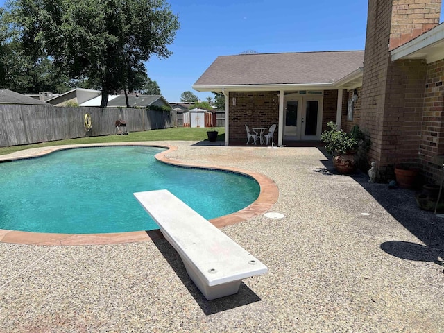 view of pool with a patio, a diving board, french doors, and a shed