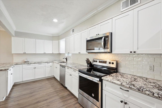 kitchen with crown molding, light hardwood / wood-style flooring, appliances with stainless steel finishes, white cabinetry, and tasteful backsplash