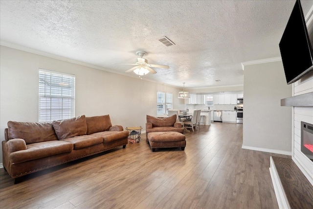 living room with hardwood / wood-style flooring, ceiling fan, ornamental molding, and a textured ceiling