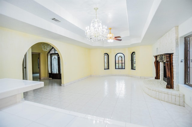 tiled living room featuring ceiling fan with notable chandelier, a stone fireplace, and a raised ceiling