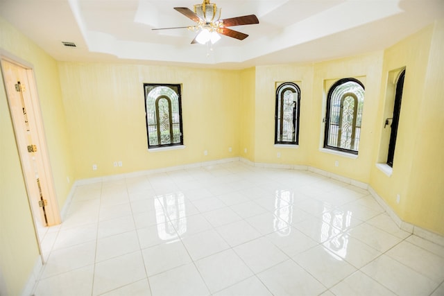 tiled empty room featuring ceiling fan and a tray ceiling