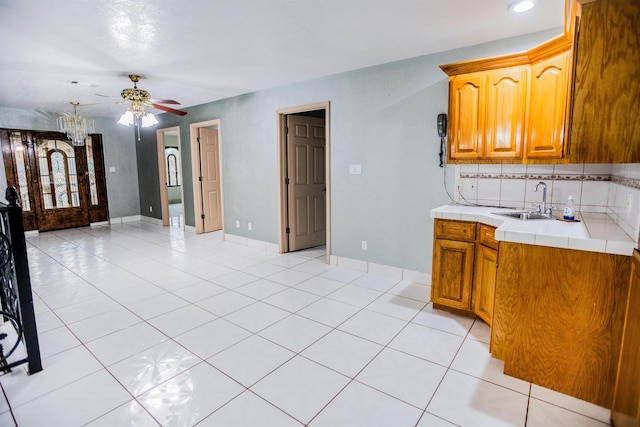 kitchen with sink, light tile patterned flooring, ceiling fan, and tile counters