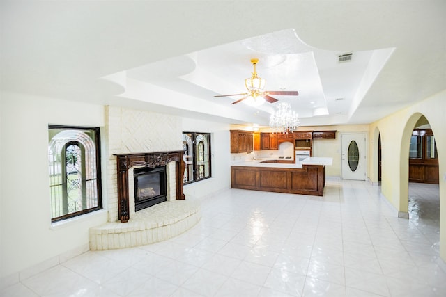 tiled living room with a tray ceiling, a notable chandelier, and a fireplace