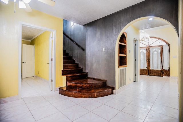 stairway with ceiling fan with notable chandelier, a textured ceiling, and tile patterned floors