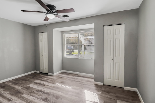 unfurnished bedroom featuring hardwood / wood-style floors, ceiling fan, and multiple closets