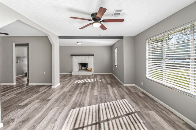 unfurnished living room with ceiling fan, a fireplace, light hardwood / wood-style floors, and a textured ceiling