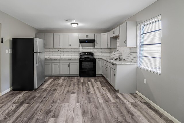 kitchen featuring sink, light stone counters, black electric range oven, backsplash, and stainless steel fridge