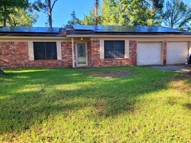 ranch-style home with a garage, solar panels, and a front lawn