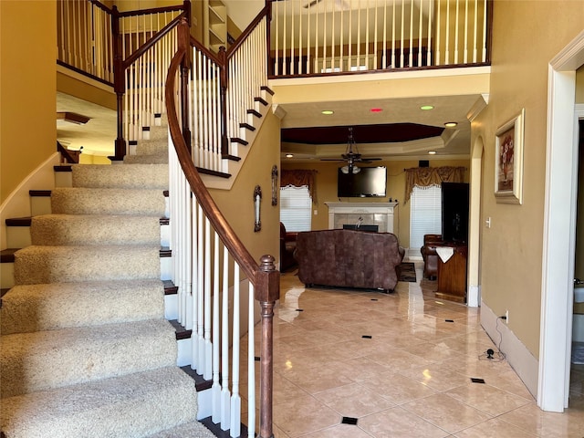 staircase with a towering ceiling, a raised ceiling, ceiling fan, and crown molding