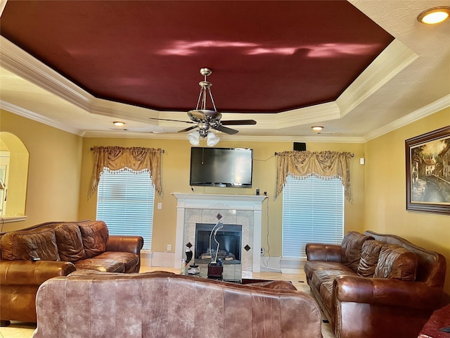 living room featuring a tile fireplace, a raised ceiling, and ornamental molding