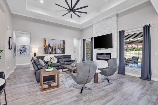 living room with ceiling fan, crown molding, light hardwood / wood-style floors, a tray ceiling, and a fireplace