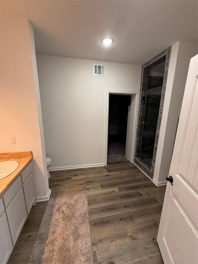 bathroom with wood-type flooring, a shower with shower door, vanity, and toilet